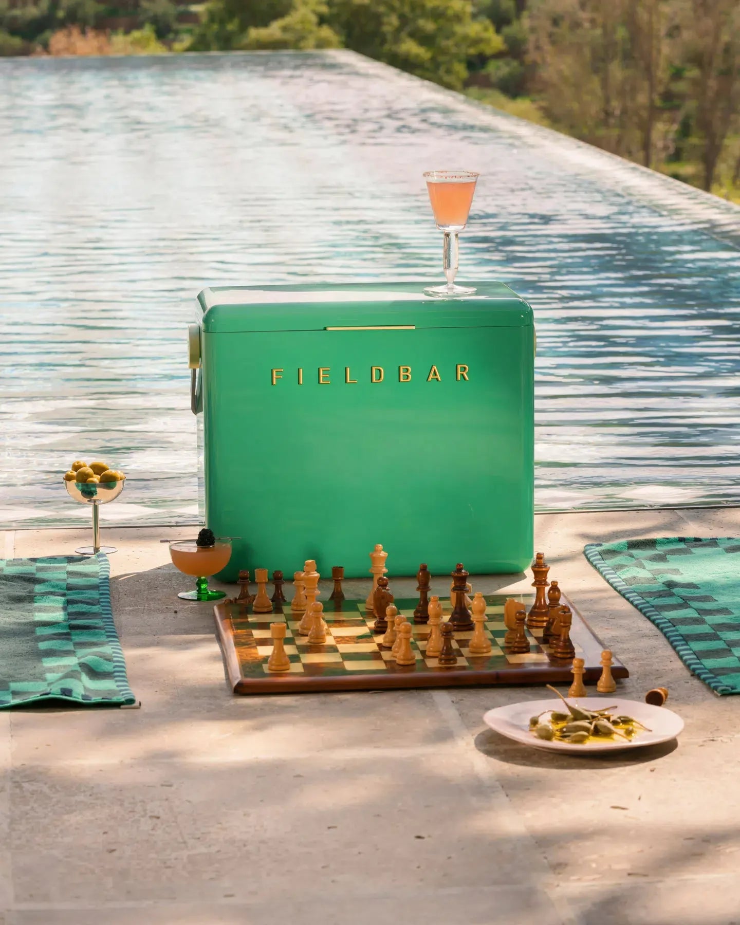 Green Fieldbar refrigerator with a chessboard and drinks on a patio with a pool view.