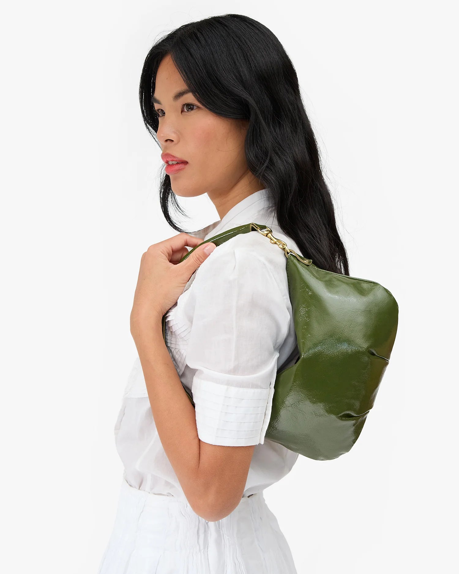 A woman in a white shirt models a green leather shoulder bag with a gold chain strap against a plain white background.