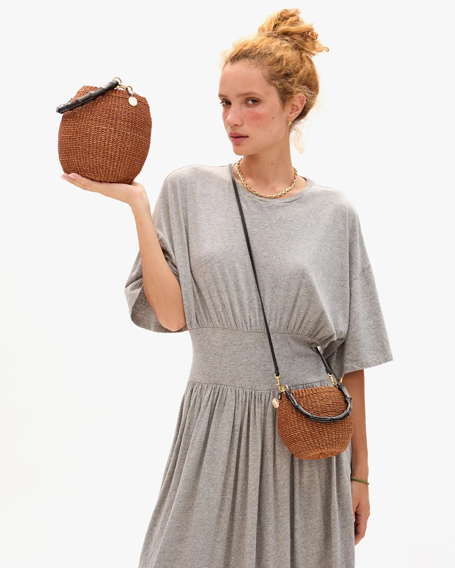 Woman holding a woven handbag and wearing a matching crossbody bag against a white background
