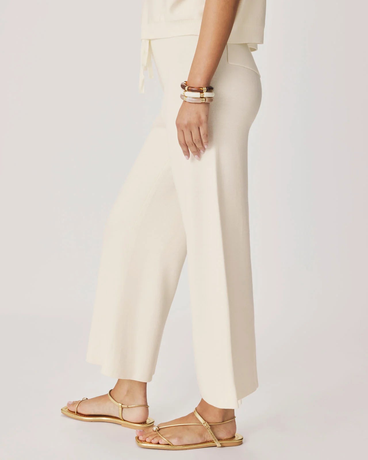 Person wearing white pants and gold sandals on a plain background