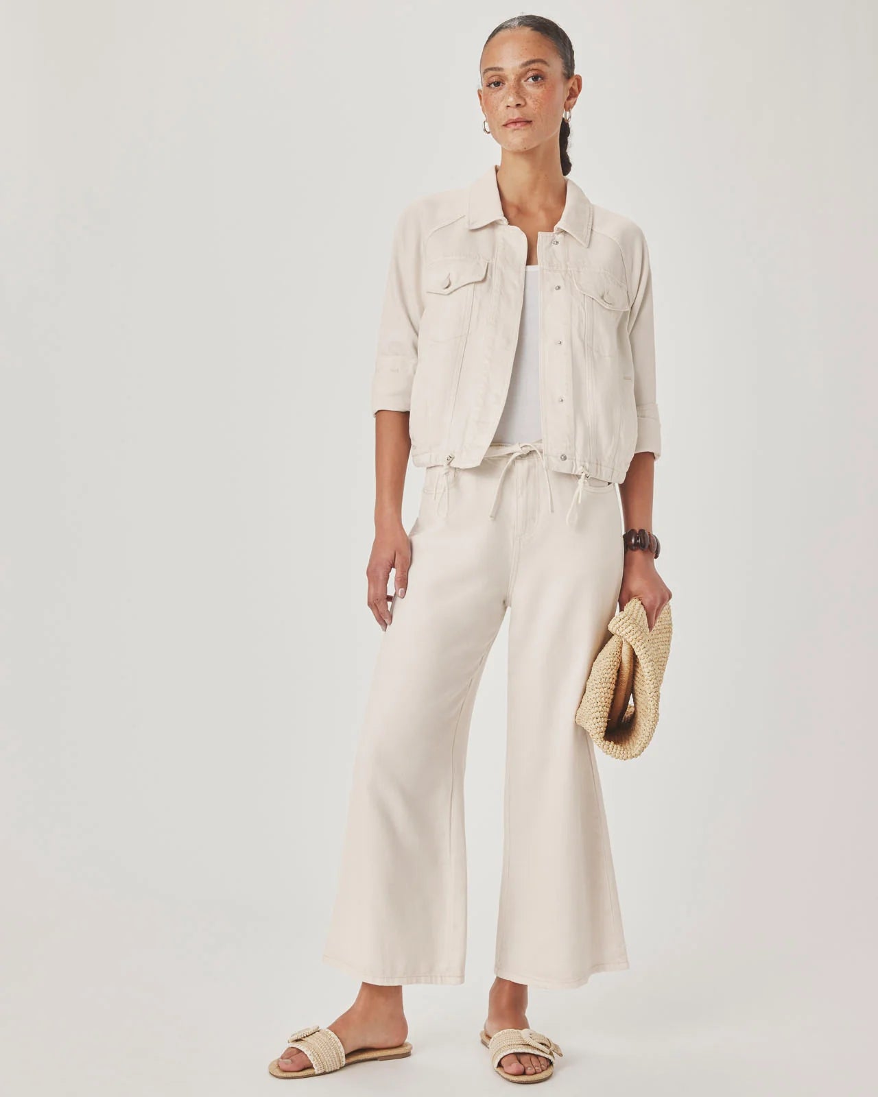 Woman wearing a beige outfit with wide-leg pants and a jacket on a white background