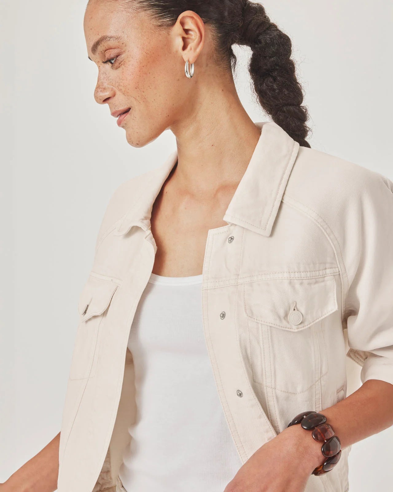 Woman wearing a beige jacket over a white top on a plain background