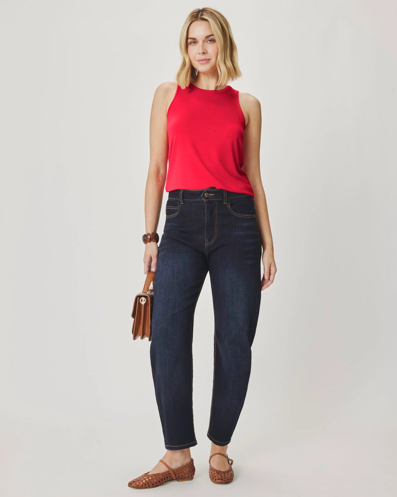 Woman wearing a red sleeveless top and dark blue jeans on a plain background