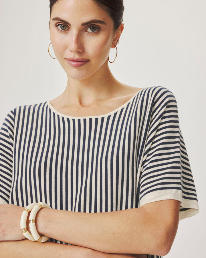 Woman wearing a black and white striped shirt with gold bracelets on a plain background