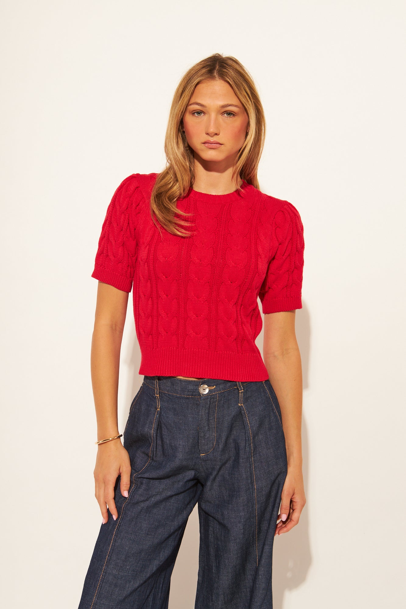 Woman wearing a red cable knit sweater and blue jeans against a white background