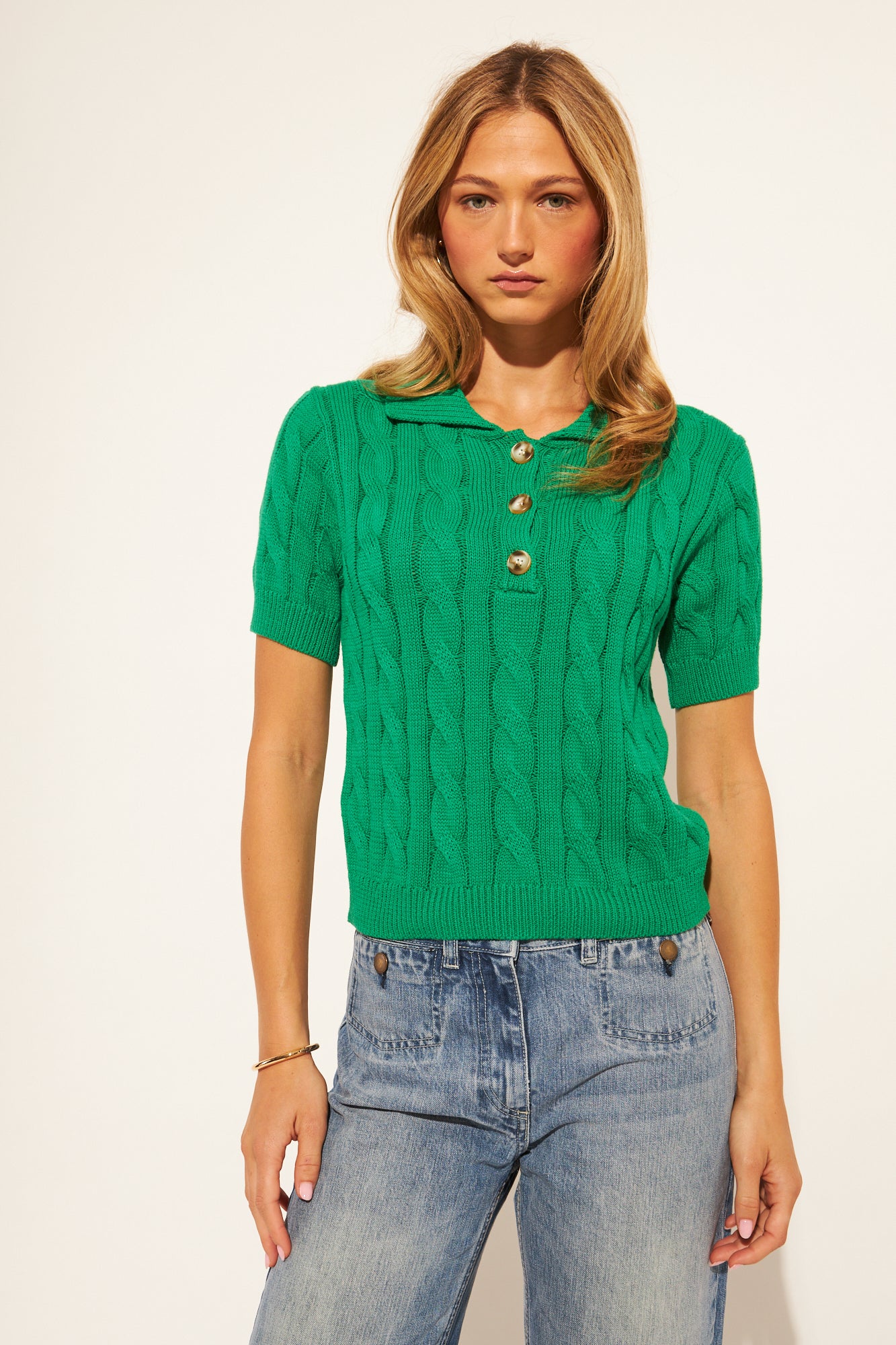 Woman wearing a green cable knit sweater and blue jeans on a white background