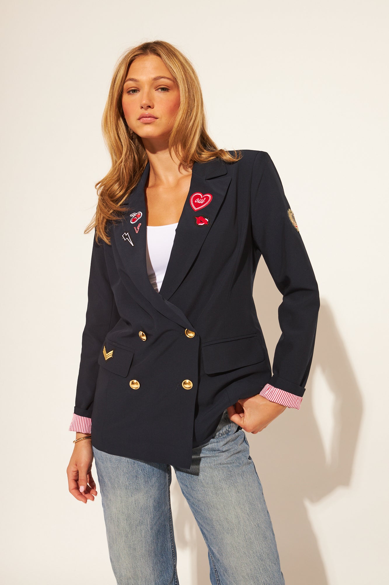 Woman wearing a navy blazer with decorative buttons and patches on a plain background