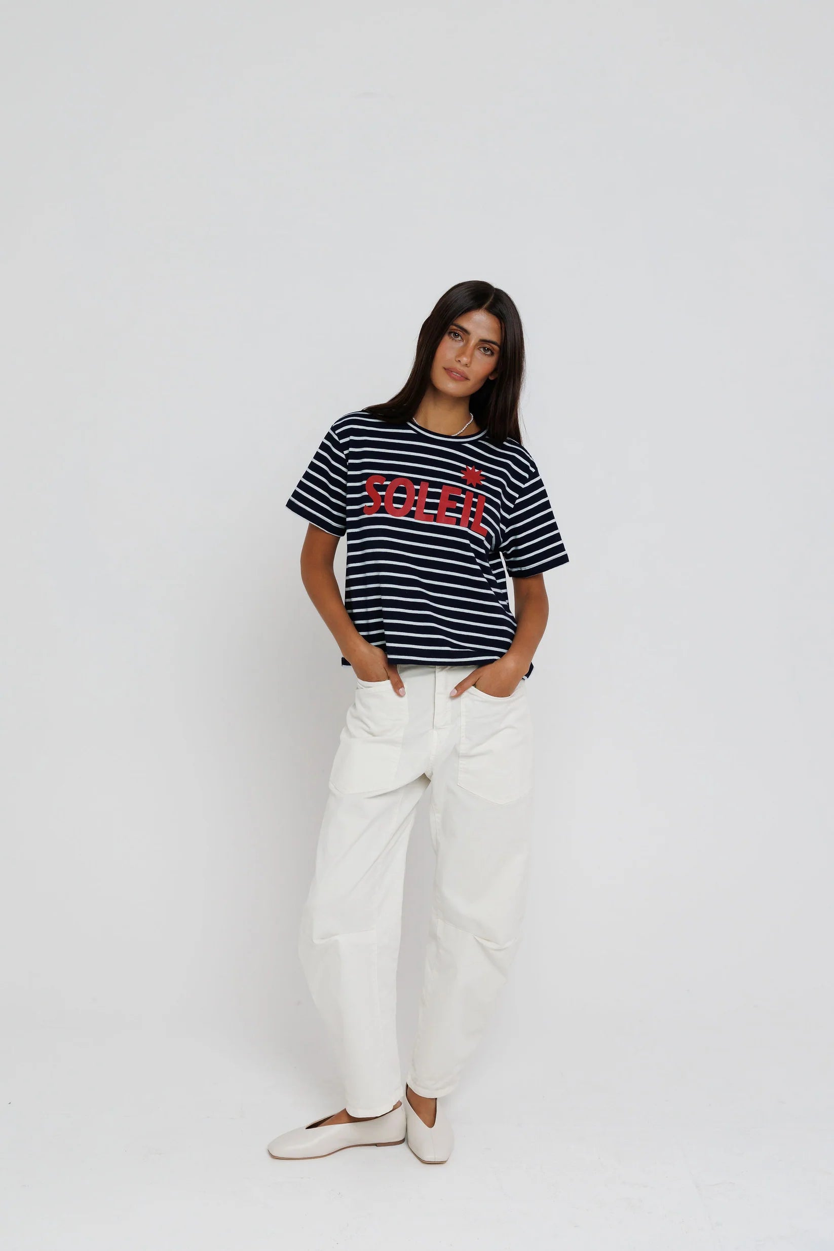 Woman wearing a striped t-shirt with a logo and white pants on a plain background
