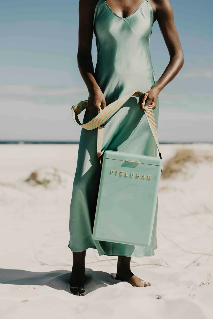 Woman in a green dress holding a matching 'Field & Co.' cooler on a beach.