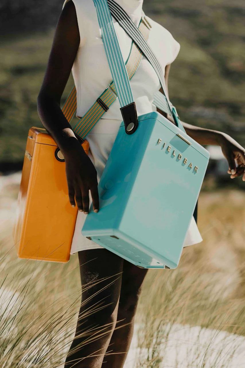 Person holding a turquoise bag with 'Fjällräven' branding in a natural setting.