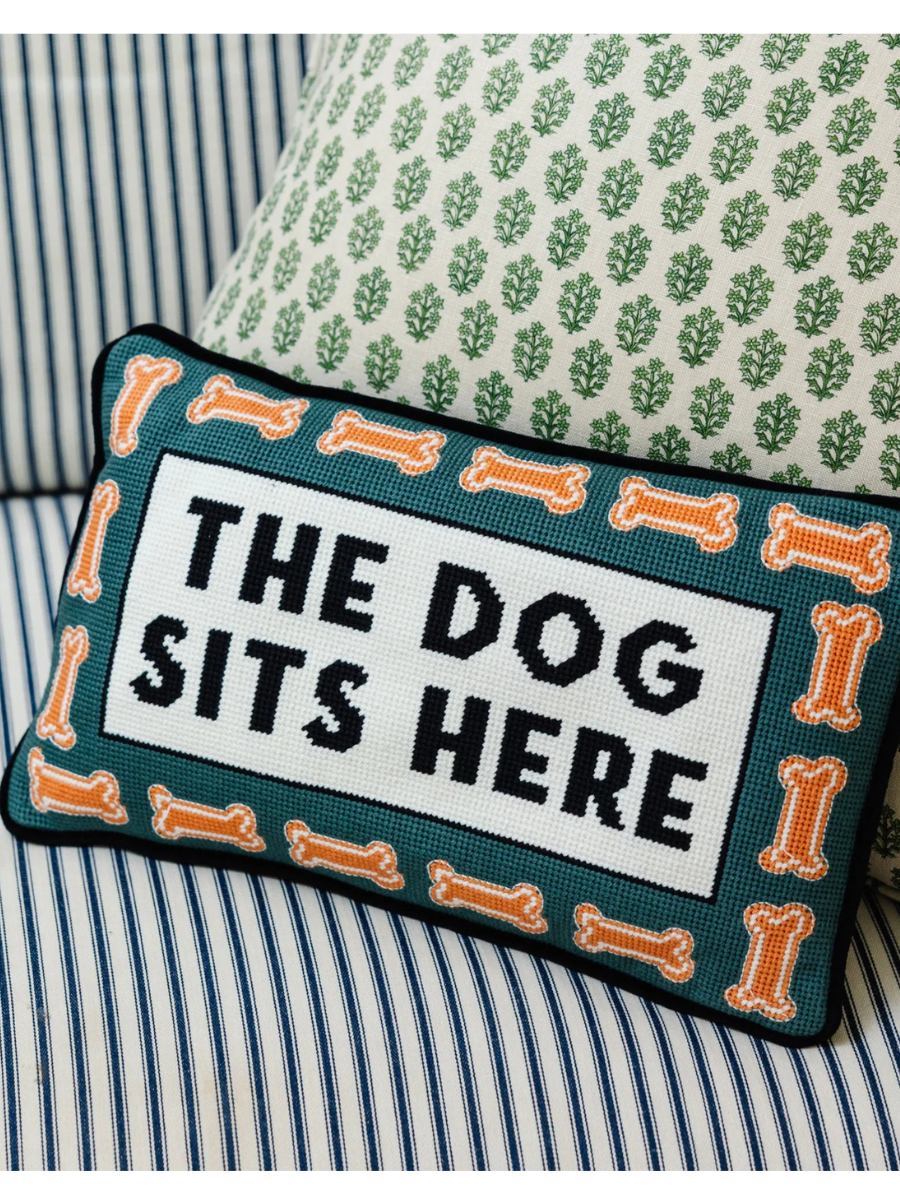Decorative pillow with 'The Dog Sits Here' text on a striped sofa.