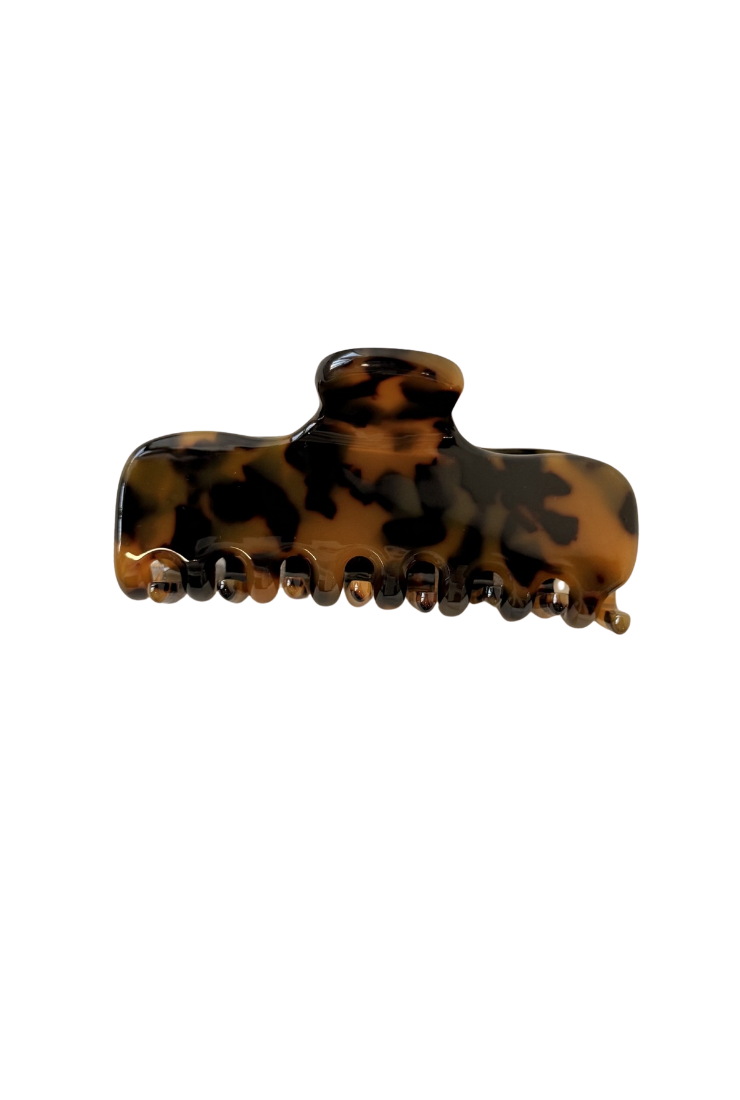 A tortoiseshell hair claw clip with a glossy finish, featuring a pattern of dark brown and amber-brown on a white background.