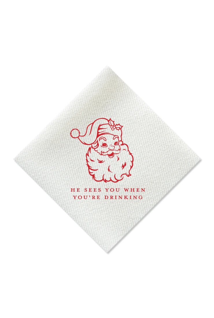 A white textured paper napkin featuring a red line-art illustration of a Santa Claus face and the humorous phrase 'HE SEES YOU WHEN YOU'RE DRINKING' printed below it.
