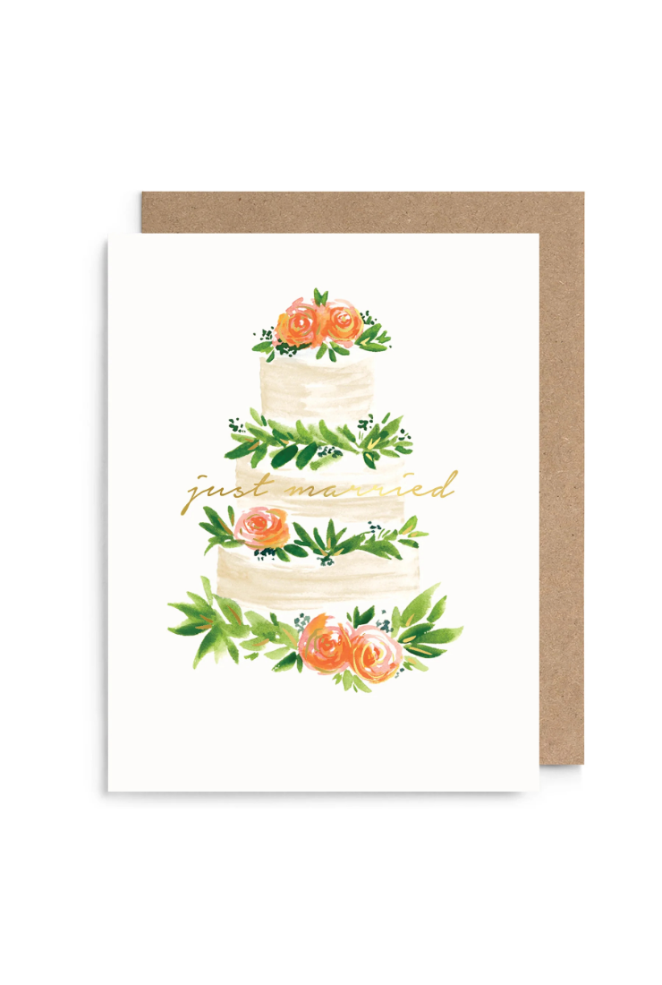 A white greeting card with a watercolor illustration of a three-tiered wedding cake decorated with green leaves and orange flowers, with the words 'just married' in gold script. A brown kraft envelope is placed behind the card on a white background.