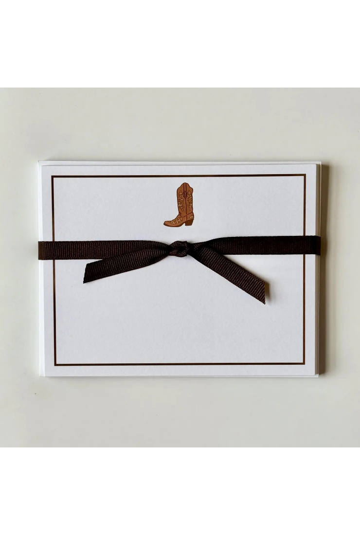 A white rectangular card or envelope with a thin brown border, featuring a small brown cowboy boot illustration near the top and wrapped with a dark brown ribbon bow, shown against a light neutral background.