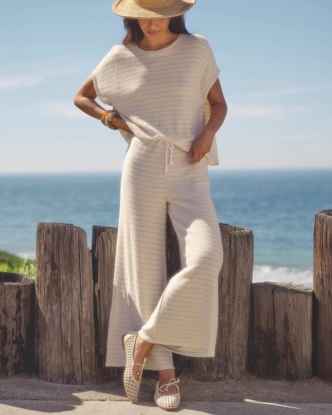 Woman in a white outfit standing by the ocean with wooden posts in the foreground