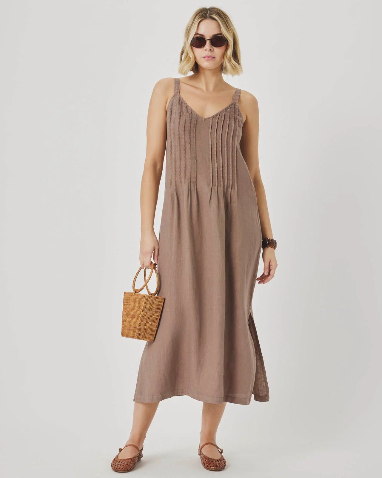 Woman wearing a brown dress holding a woven bag on a white background