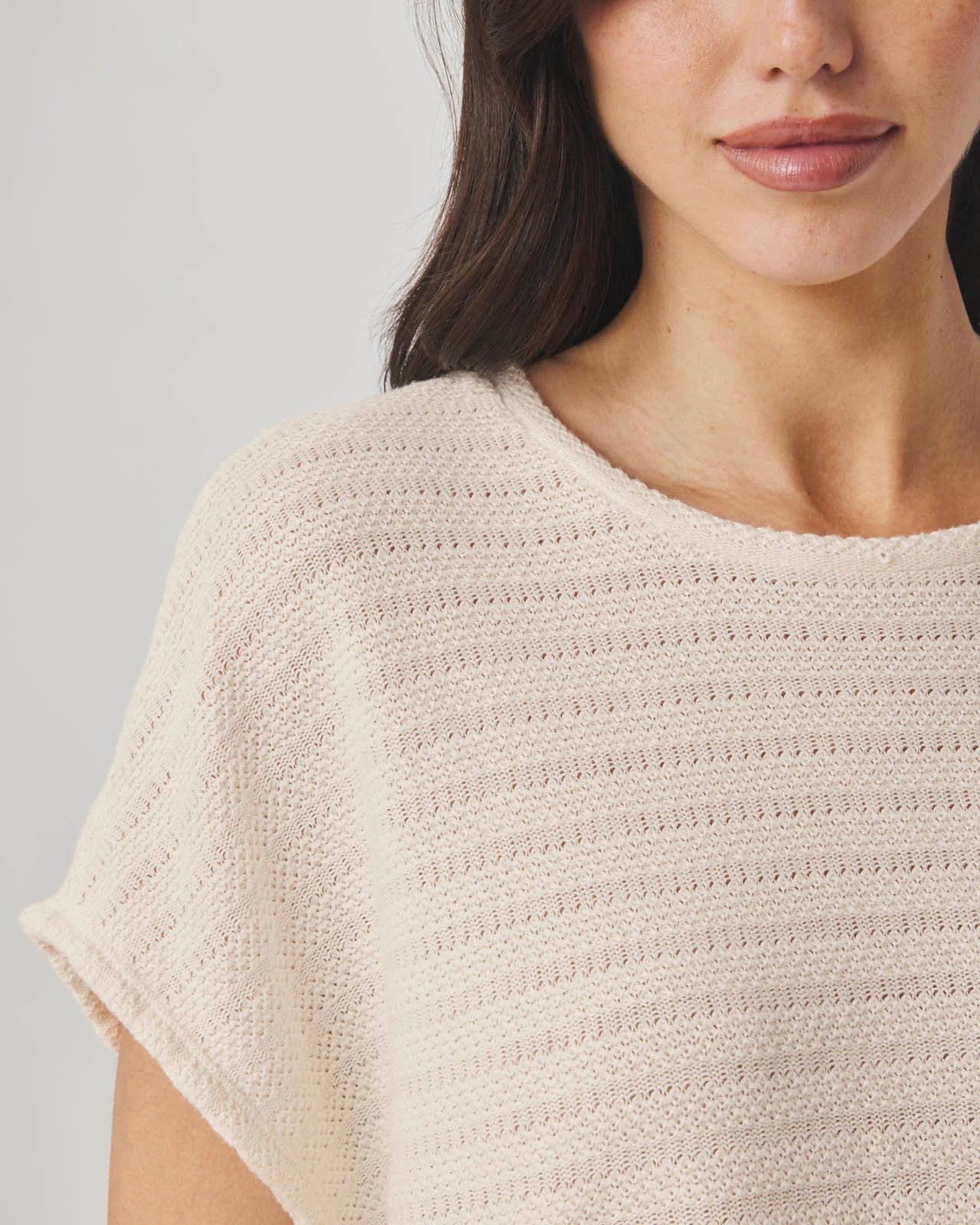 Close-up of a person wearing a beige knit poncho against a neutral background