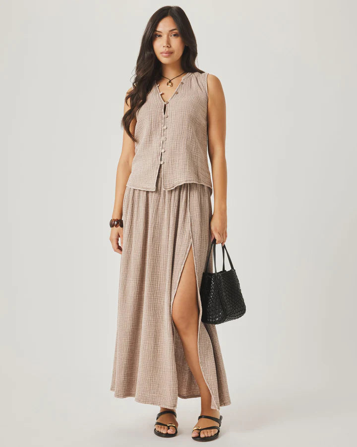 Woman wearing a sleeveless beige top and long skirt with a black handbag on a white background