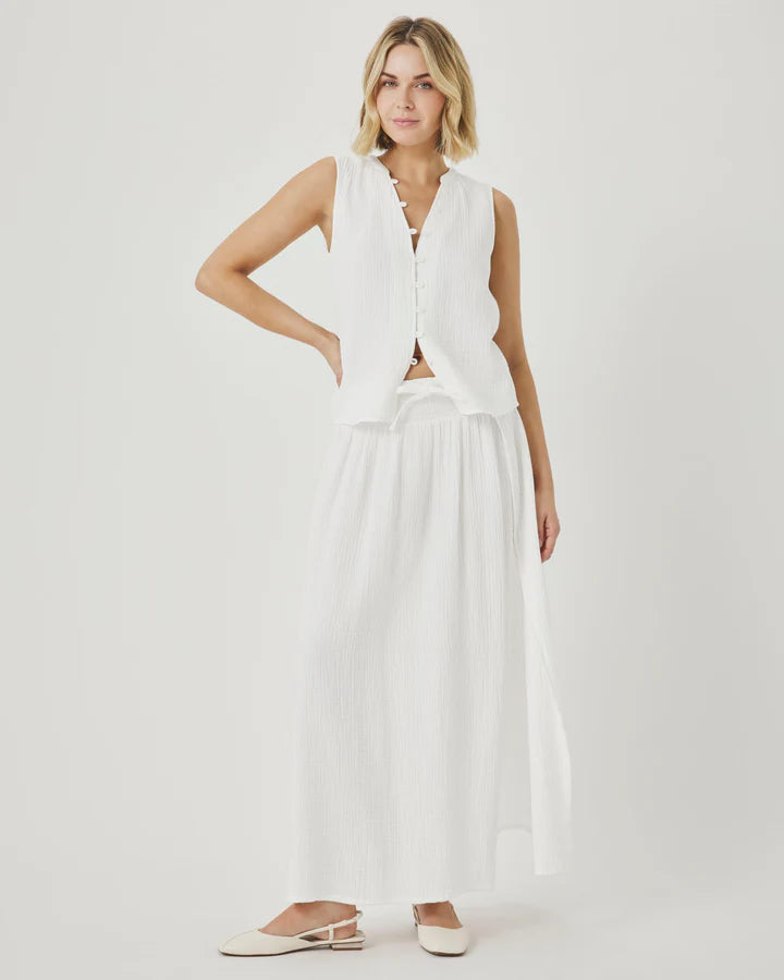 Woman wearing a white sleeveless top and wide-leg pants on a light background