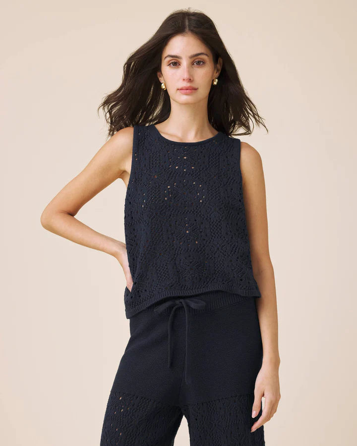 Woman wearing a dark blue sleeveless top and pants on a beige background