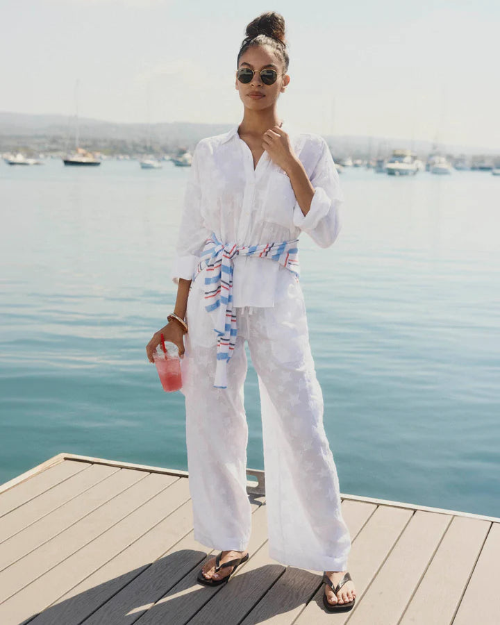 Woman in white outfit with colorful belt standing on a dock by the water