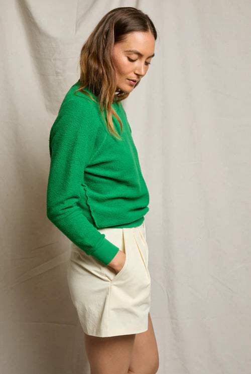 Woman wearing a green sweater and white shorts against a plain background