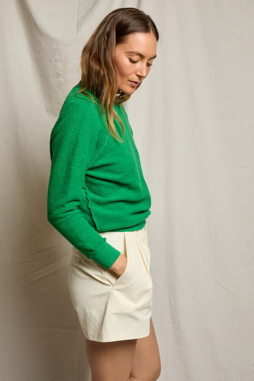 Woman wearing a green sweater and white shorts against a plain background