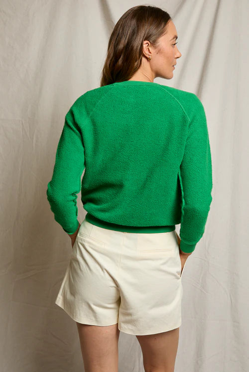 Person wearing a green sweater and white shorts against a plain background