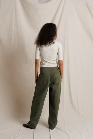 Person wearing a white top and green pants standing against a plain background