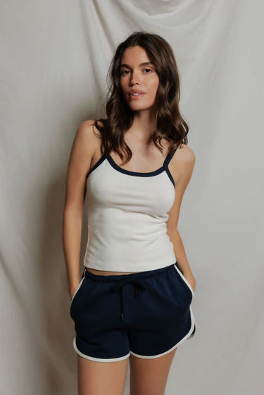 Woman wearing a white tank top with navy trim and navy shorts against a plain background