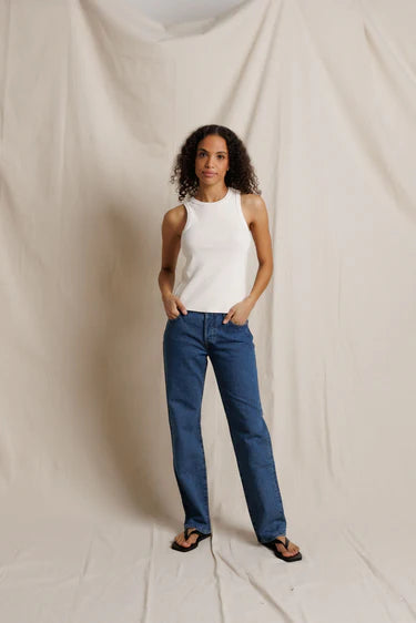 Woman wearing a white sleeveless top and blue jeans against a plain background