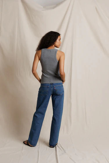 Person wearing a gray tank top and blue jeans standing against a plain background
