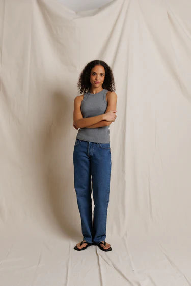 Woman wearing a gray tank top and blue jeans standing against a plain background