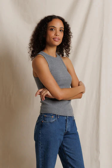 Woman wearing a gray sleeveless top and blue jeans against a beige background
