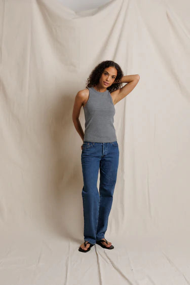 Woman wearing a gray tank top and blue jeans standing against a beige backdrop