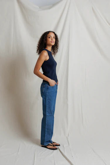 Woman wearing a navy tank top and blue jeans standing against a plain white background