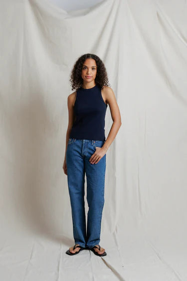 Woman wearing a navy tank top and blue jeans standing against a plain white background