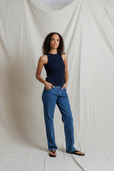 Woman wearing a navy tank top and blue jeans standing against a plain white background