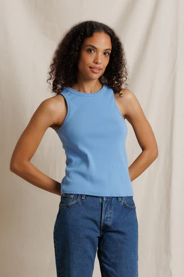 Woman wearing a blue sleeveless top and jeans against a beige background