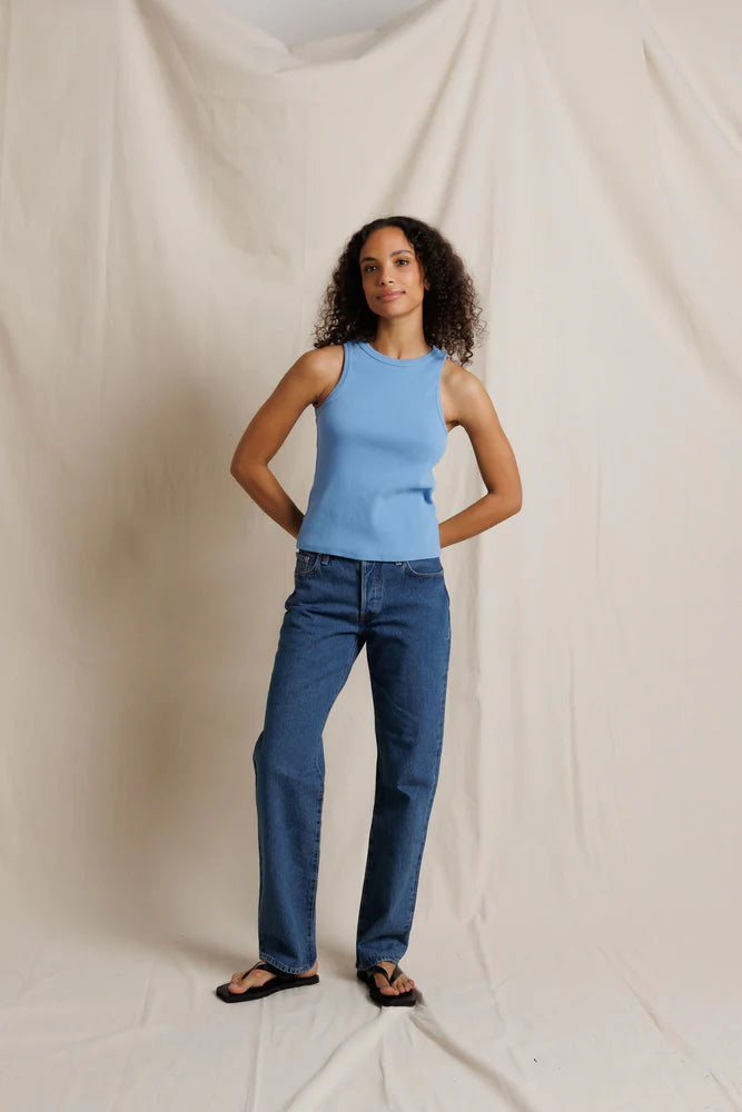 Woman wearing a light blue sleeveless top and dark blue jeans against a plain background