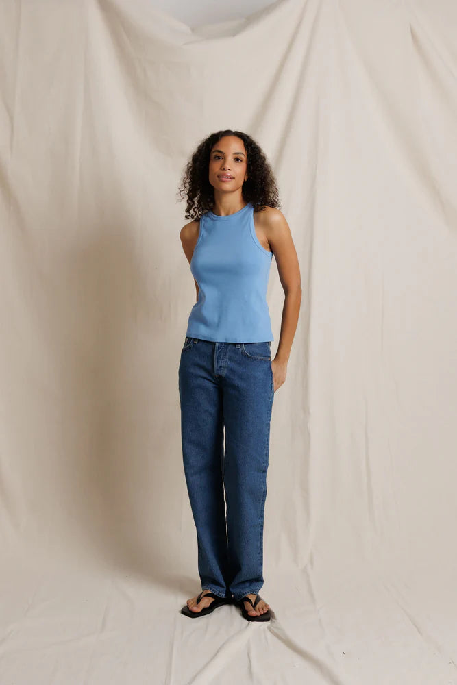 Woman wearing a blue top and jeans standing against a plain background