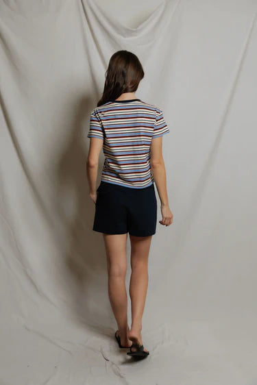 Person wearing a striped shirt and dark shorts standing against a plain white backdrop