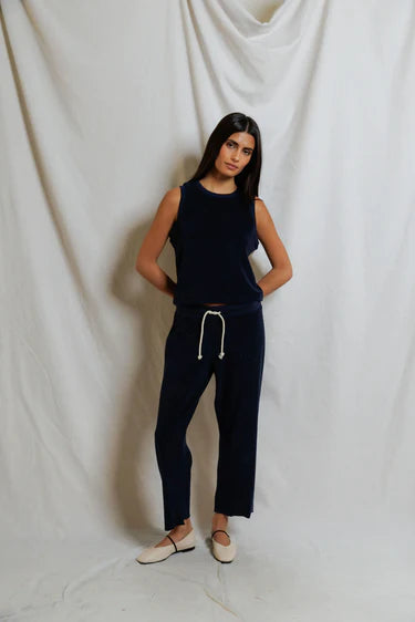 Woman wearing a navy sleeveless top and pants against a white draped curtain background