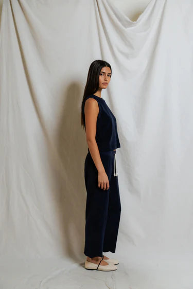 Woman wearing a navy blue sleeveless top and wide-leg pants against a white curtain backdrop