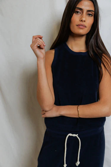 Woman wearing a navy sleeveless top and dark pants against a plain background