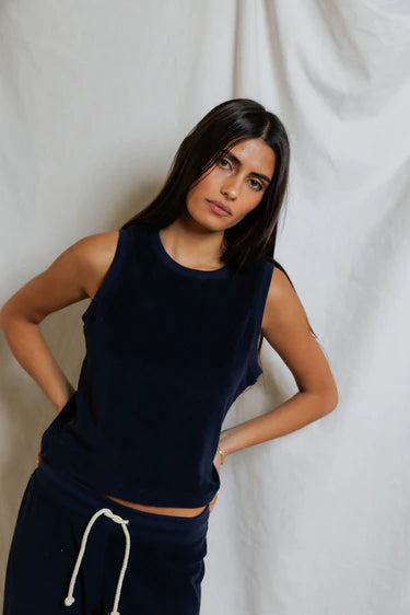 Woman wearing a navy sleeveless top and dark pants against a plain background