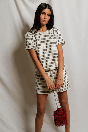 Woman wearing a striped outfit holding a red bag against a plain background
