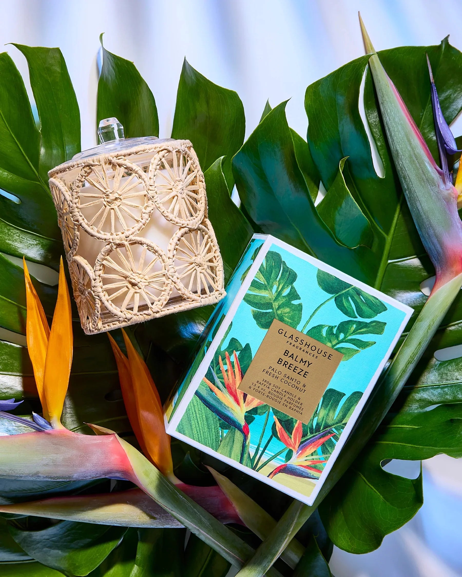 Decorative candle with wicker cover and packaging on tropical leaves