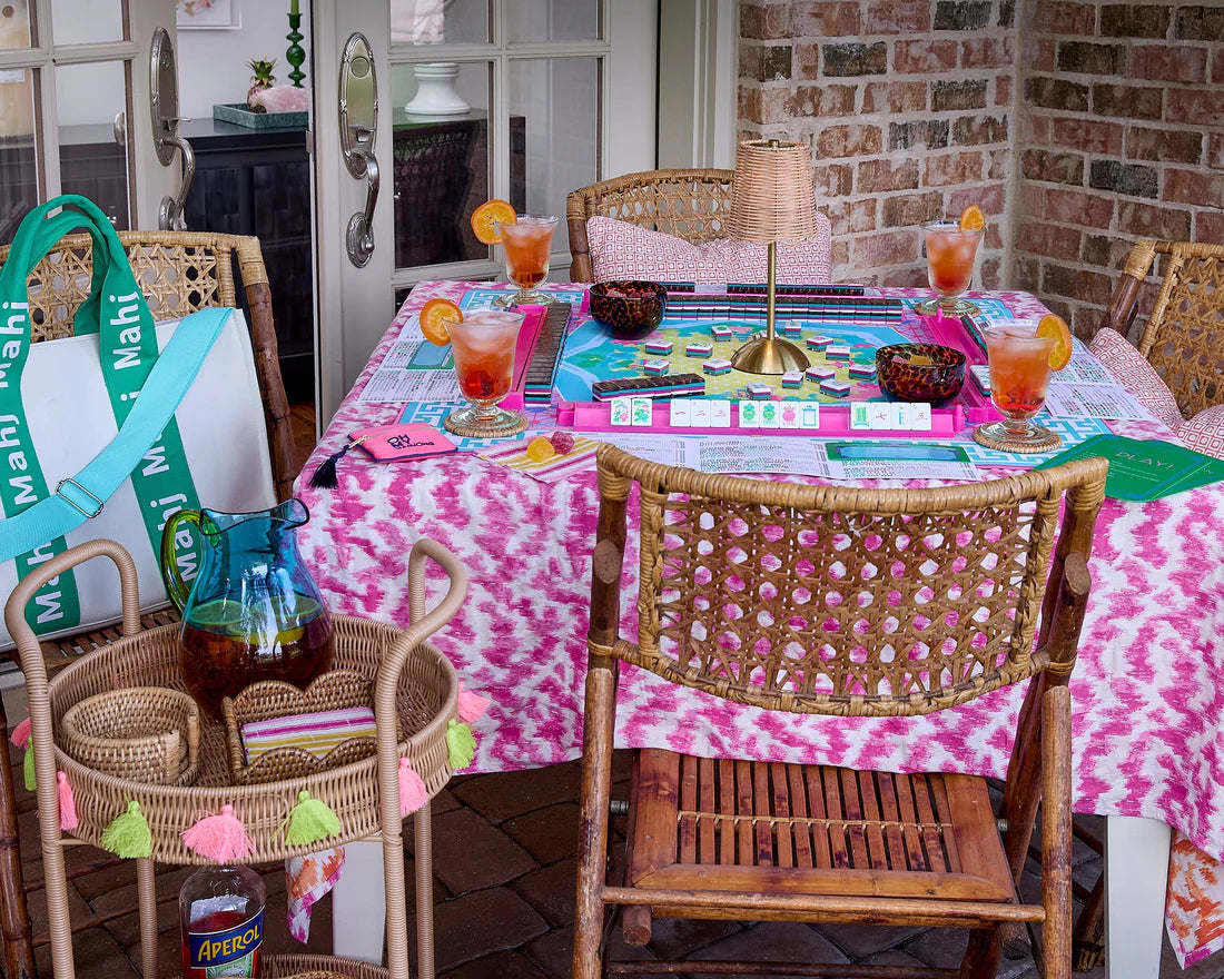 Outdoor dining setup with a pink and white tablecloth, drinks, and cards on a patio.